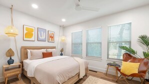 Une chambre à coucher moderne avec un lit en bois, une petite table de chevet, une chaise et une grande fenêtre avec des stores.