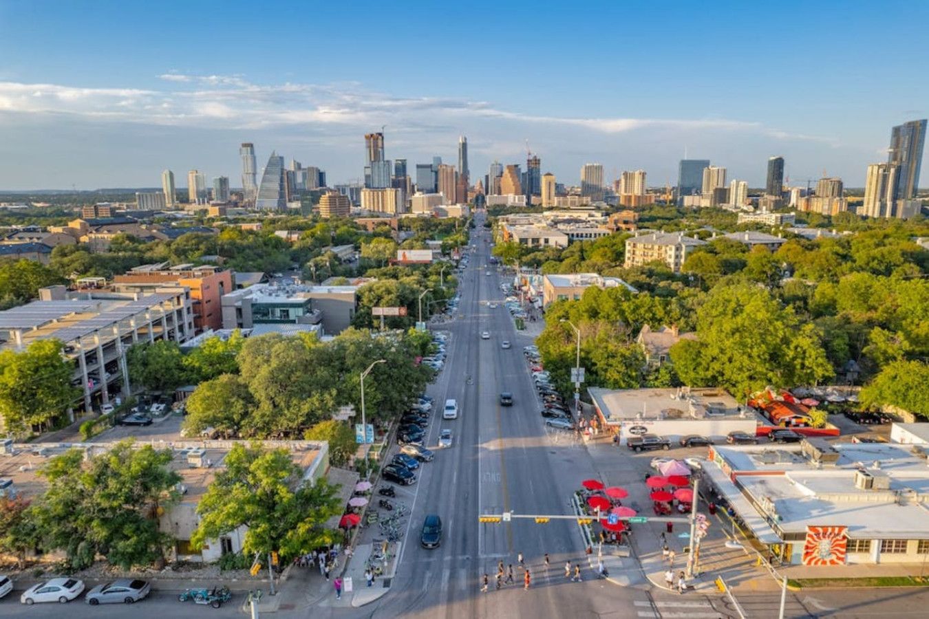 A cityscape with a wide road, buildings, and greenery.