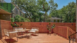 Une terrasse en bois avec des meubles d’extérieur, une clôture en bois et des arbres en arrière-plan.