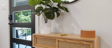 Una consola de madera con una planta y una lámpara, ubicada al lado de una puerta negra con paneles de vidrio.