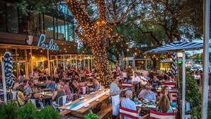 Un espace de restauration en plein air avec des tables et des chaises en bois, entouré de verdure et illuminé de guirlandes lumineuses.