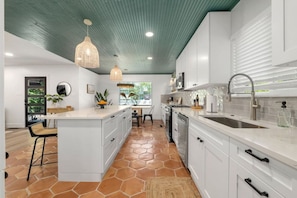 A modern kitchen with white cabinets, a large island, and a stone tile floor.
