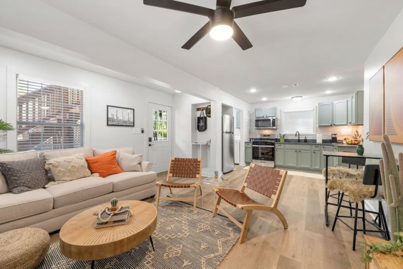 A modern living room with a sofa, armchairs, and a coffee table. There is a kitchen area with cabinets and appliances.