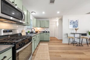 A modern kitchen with green cabinets, a stainless steel stove, and a dining area with two stools.