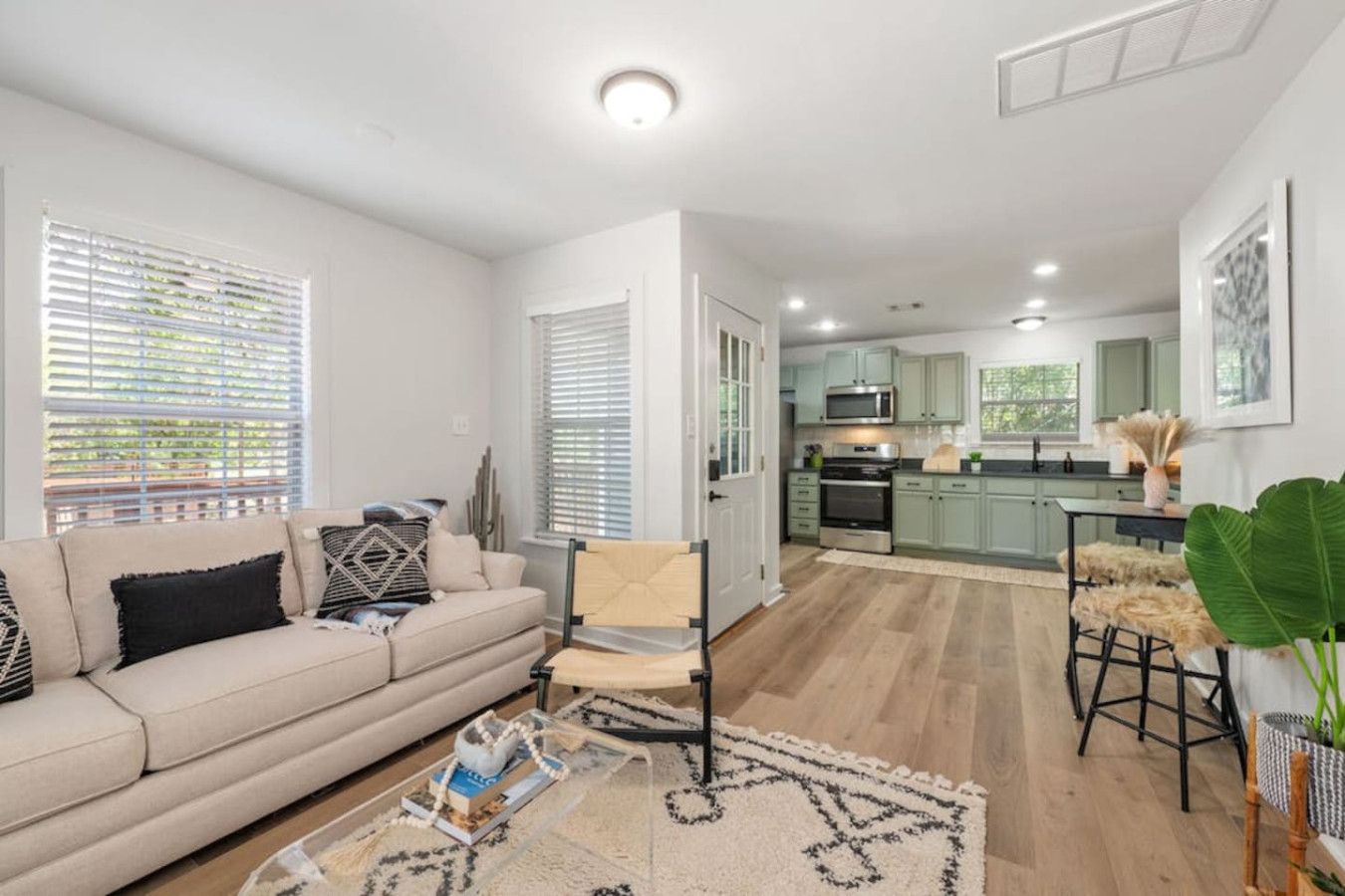 A modern living room with a sofa, a coffee table, and a chair. There is a kitchen area with a microwave, stove, and bar stools.