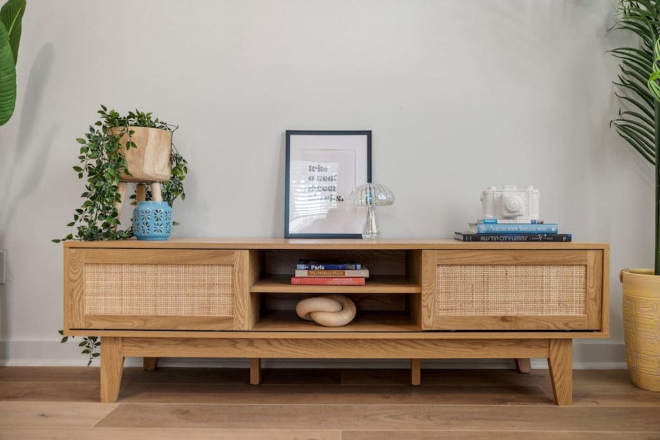 A wooden console table with wicker storage compartments, a framed picture, and decorative items.