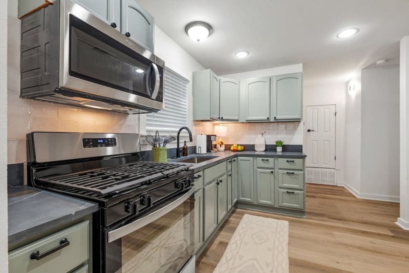 A modern kitchen with stainless steel appliances, light green cabinets, and a wooden floor.