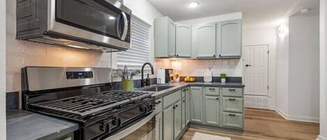 Una cocina moderna con electrodomésticos de acero inoxidable, armarios verde claro y piso de madera.