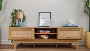 Une console en bois dotée de compartiments de rangement en osier, d’un tableau encadré et d’objets décoratifs.