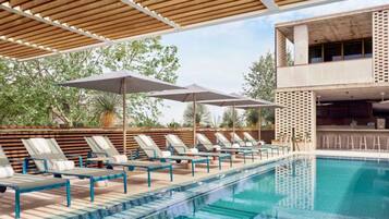 Area piscina con lettini e ombrelloni, una piscina cristallina e una moderna struttura edilizia sullo sfondo.