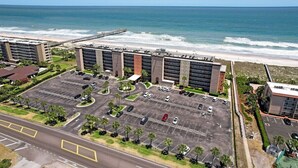 Un hôtel situé sur la côte, doté d’un parking, offrant une vue sur la plage et avec une jetée en arrière-plan.