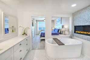 Une salle de bain moderne avec une baignoire sur pieds, un grand miroir et un téléviseur fixé au mur.