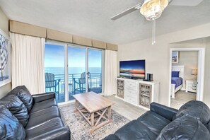Un salon avec un canapé, une table basse et un téléviseur. Il y a un balcon avec vue sur l’océan.