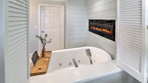 A modern bathroom with a freestanding bathtub, a wall-mounted fireplace, and a wooden side table with a vase. - Oceanfront | King + Balcony +Jetted Soaking Tub (Daytone Beach)