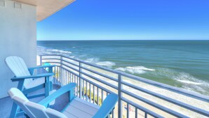 A balcony with a view of the ocean, featuring two blue chairs and a small table. - Oceanfront | King + Balcony +Jetted Soaking Tub (Daytone Beach)