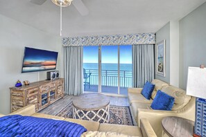 A hotel room with a balcony, a television, a sofa, a coffee table, and a patterned curtain. - Oceanfront | King + Balcony +Jetted Soaking Tub (Daytone Beach)