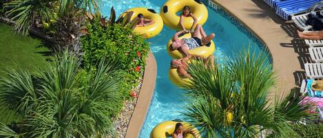A swimming pool with inflatable rings, lounge chairs, and palm trees.