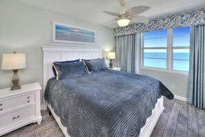 A bedroom with a bed, nightstands, a ceiling fan, a painting, and a view of the ocean. - Oceanfront | King + Balcony +Jetted Soaking Tub (Daytone Beach)