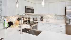 Uma cozinha moderna com armários brancos, eletrodomésticos de aço inoxidável, uma pia dupla e painel de azulejos.