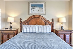 A bedroom with a large bed, two bedside tables, a wooden headboard, and a framed picture on the wall. - Oceanfront Escape | King Bed + 2 Balconies (Daytona Beach)