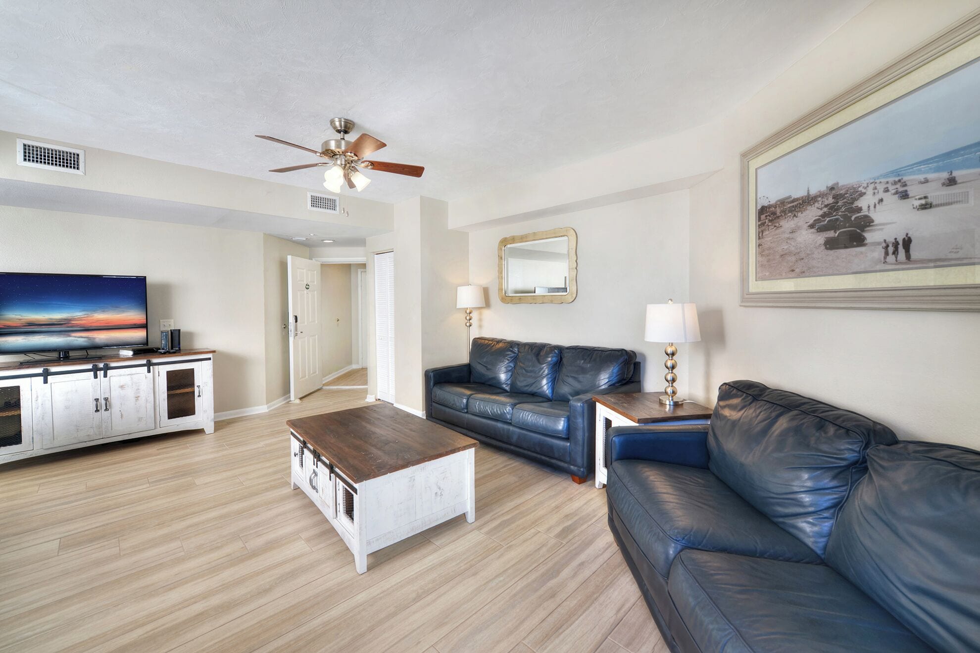 A living room with a television, leather sofas, a coffee table, and a ceiling fan.