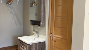 A bathroom with a wooden vanity, a mirror, and a door. - Lugano Arte Homestay (Jakarta)