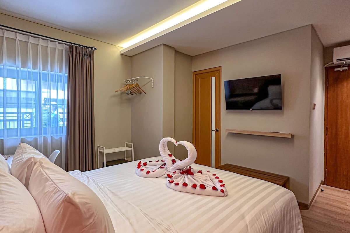 A hotel room with a large bed, a TV mounted on the wall, and a window with curtains.
