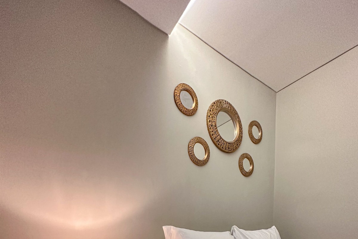 A neatly made bed with white bedding, a bedside table with a lamp, and decorative wall art.