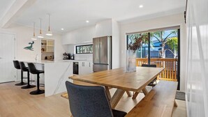 A modern kitchen with white cabinets, a stainless steel refrigerator, and a wooden dining table with benches. - Another on Leo! (Waihi Beach)