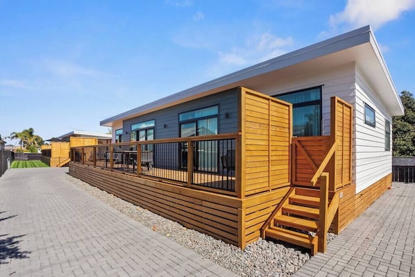 A modern building with a flat roof, large windows, and a wooden deck area. - Another on Leo! (Waihi Beach)