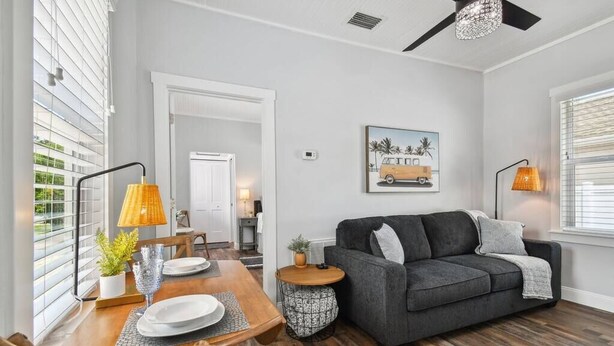 A living room with a dark grey sofa, wooden dining table, and a ceiling fan. - Downtown Dunedin Hideaway / Easy Walk to Downtown! (Dunedin)