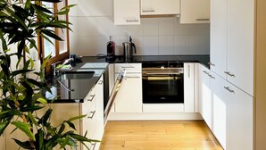 A modern kitchen with white cabinets, a black countertop, and a wooden floor. - MAISONETTE 4.5 rooms, near Ballenberg, ski areas, playground, BeO ApartmentsAG (Hofstetten bei Brienz)