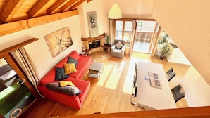 A spacious living area with a red sofa, a fireplace, and a dining table. - MAISONETTE 4.5 rooms, near Ballenberg, ski areas, playground, BeO ApartmentsAG (Hofstetten bei Brienz)