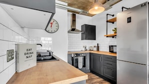 A modern kitchen with a stainless steel refrigerator, a clock, and a book titled "EAT DRINK NAP". - Wembley Park Apartments (Wembley)