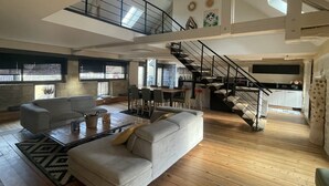 A spacious living area with a high ceiling, a staircase, and a kitchen area. - Duplex Dans le Centre Ville de Sarlat-la-canéda (Sarlat-la-Canéda)