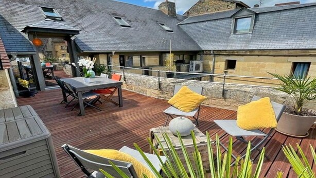 A covered outdoor patio with seating and a table, stone walls, and a sloped roof. - Duplex Dans le Centre Ville de Sarlat-la-canéda (Sarlat-la-Canéda)