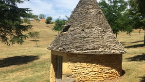 A small stone hut with a conical roof, surrounded by grassy fields and trees. - Duplex Dans le Centre Ville de Sarlat-la-canéda (Sarlat-la-Canéda)