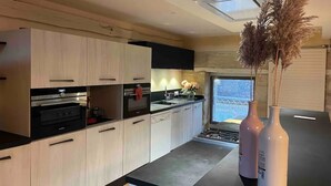 A modern kitchen with light wood cabinets, black countertops, and a built-in oven. There are two white vases with dried plants on the counter. - Duplex Dans le Centre Ville de Sarlat-la-canéda (Sarlat-la-Canéda)