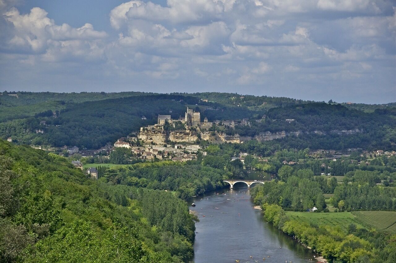 Un château historique perché sur une colline, dominant une rivière qu’enjambe un pont.