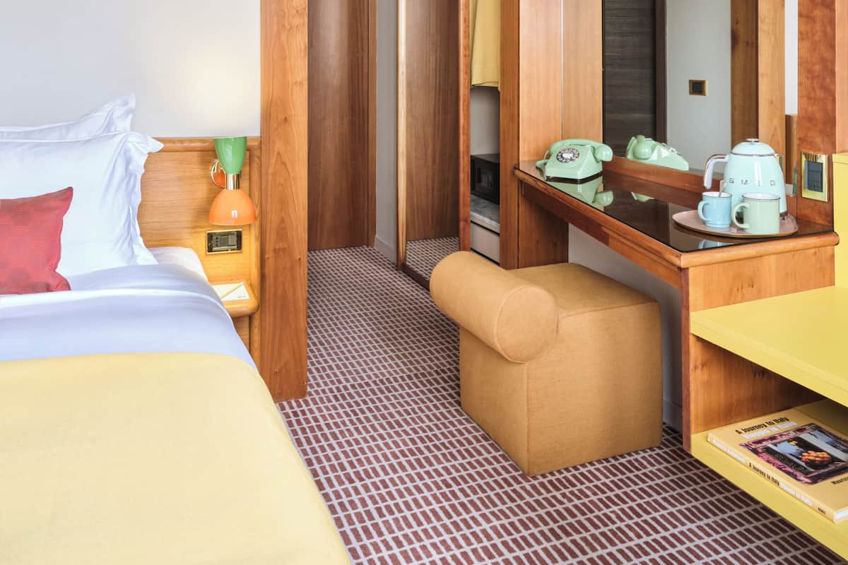 A hotel room with a bed, a desk, a chair, a mirror, and a wardrobe.