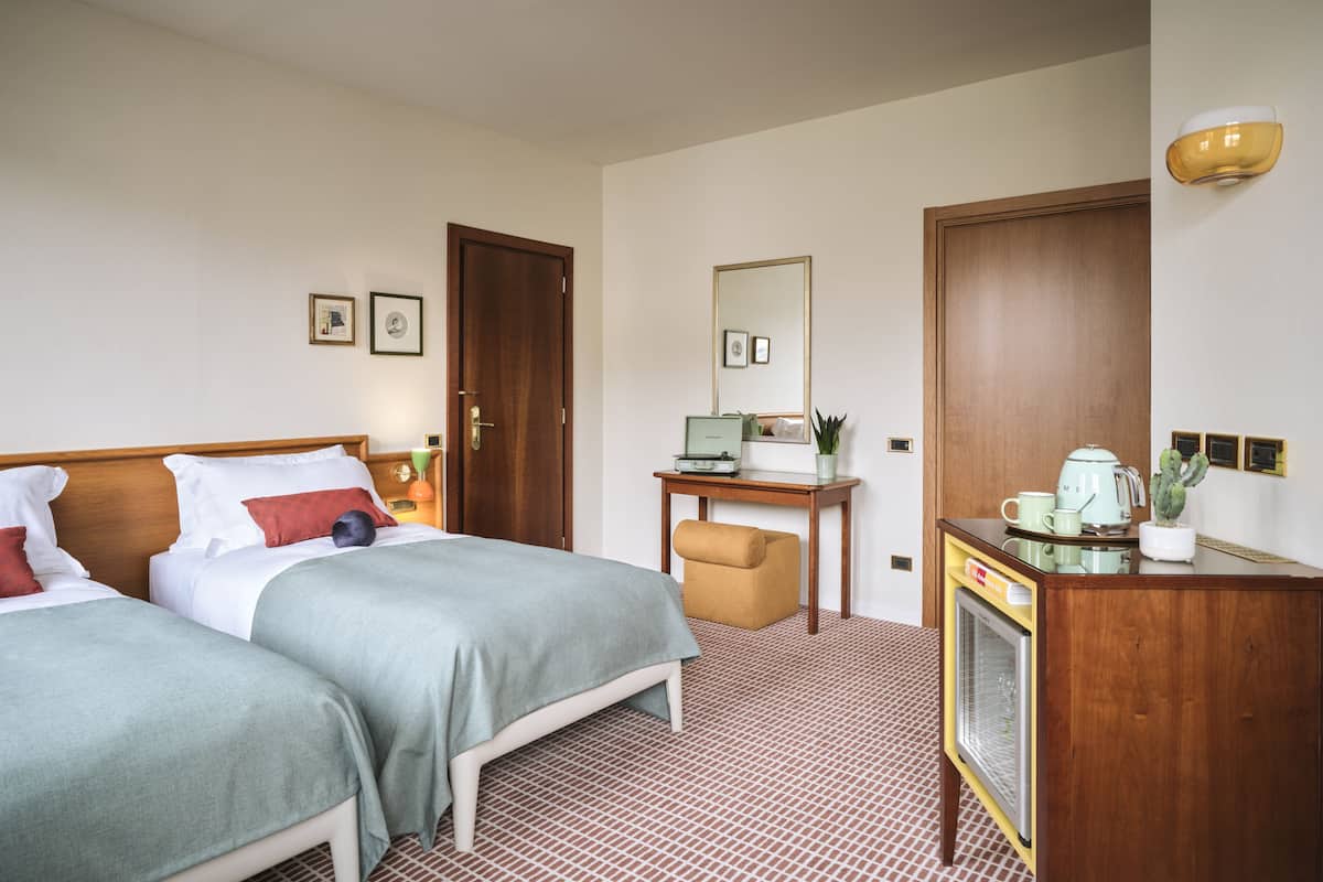 A hotel room with two beds, a desk with a computer, a chair, a coffee maker, and a television.