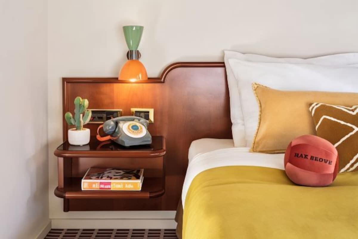 A neatly made bed with a yellow bedspread, a pillow with a geometric pattern, and a red sports ball on the bed.