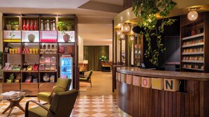 A hotel lobby with a check-in counter, seating area, and a variety of amenities including a beverage dispenser and shelves stocked with snacks and toiletries. - Max Brown Hotel Missori, part of Sircle Collection (Milan)