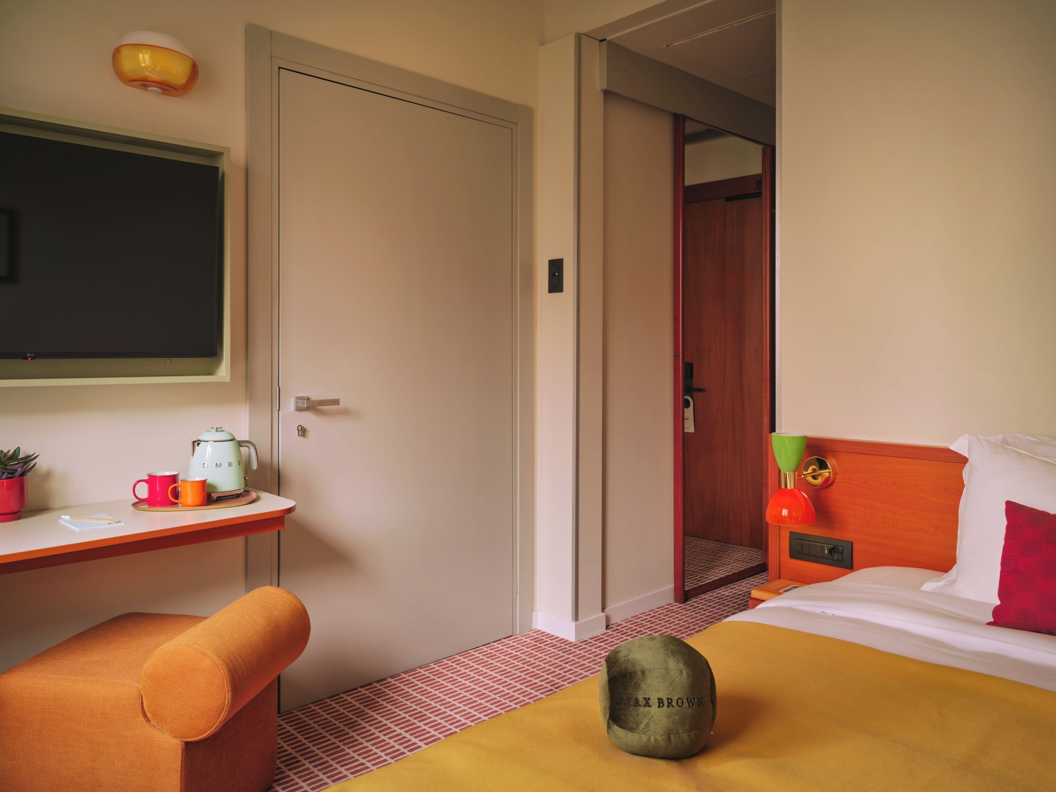 Ein Hotelzimmer mit einem Bett, einem Schreibtisch mit Wasserkocher, einem Sessel und einer Tür zu einem weiteren Raum.