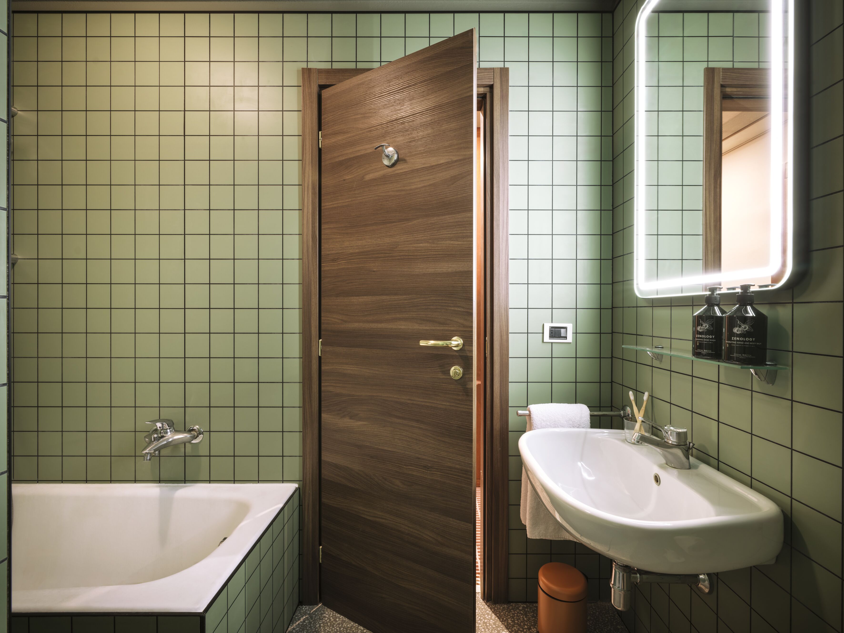 Een badkamer met een houten deur, een witte wastafel en een bad.