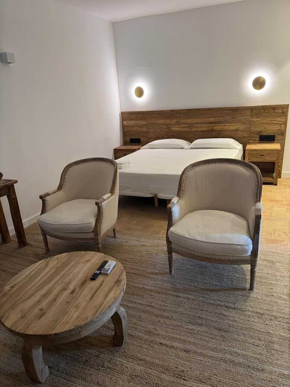 Un dormitorio con una cama, dos sillones y una pequeña mesa de madera.