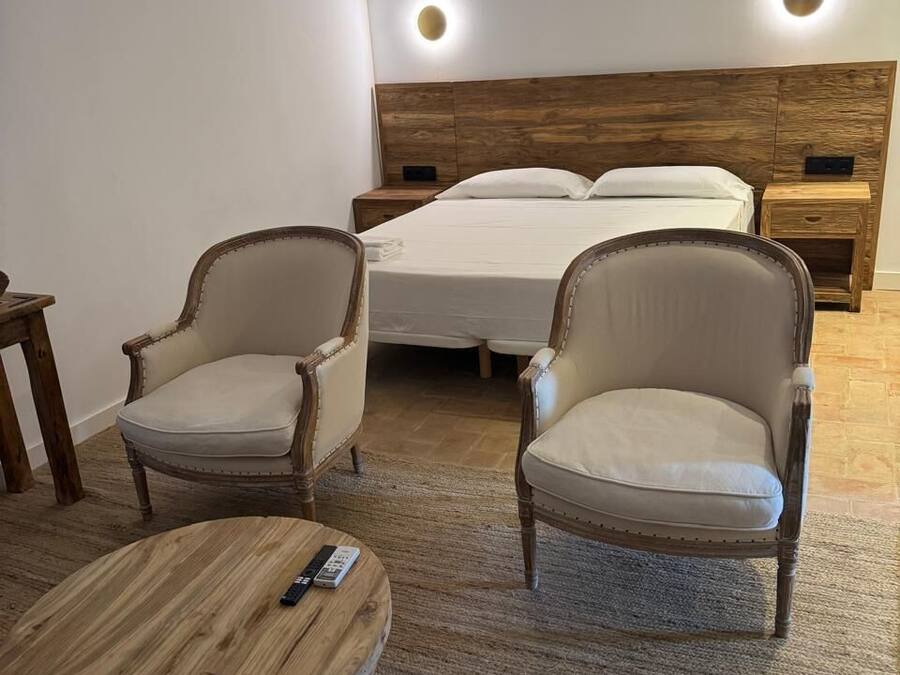 Un dormitorio con una cama, dos sillones y una pequeña mesa de madera.