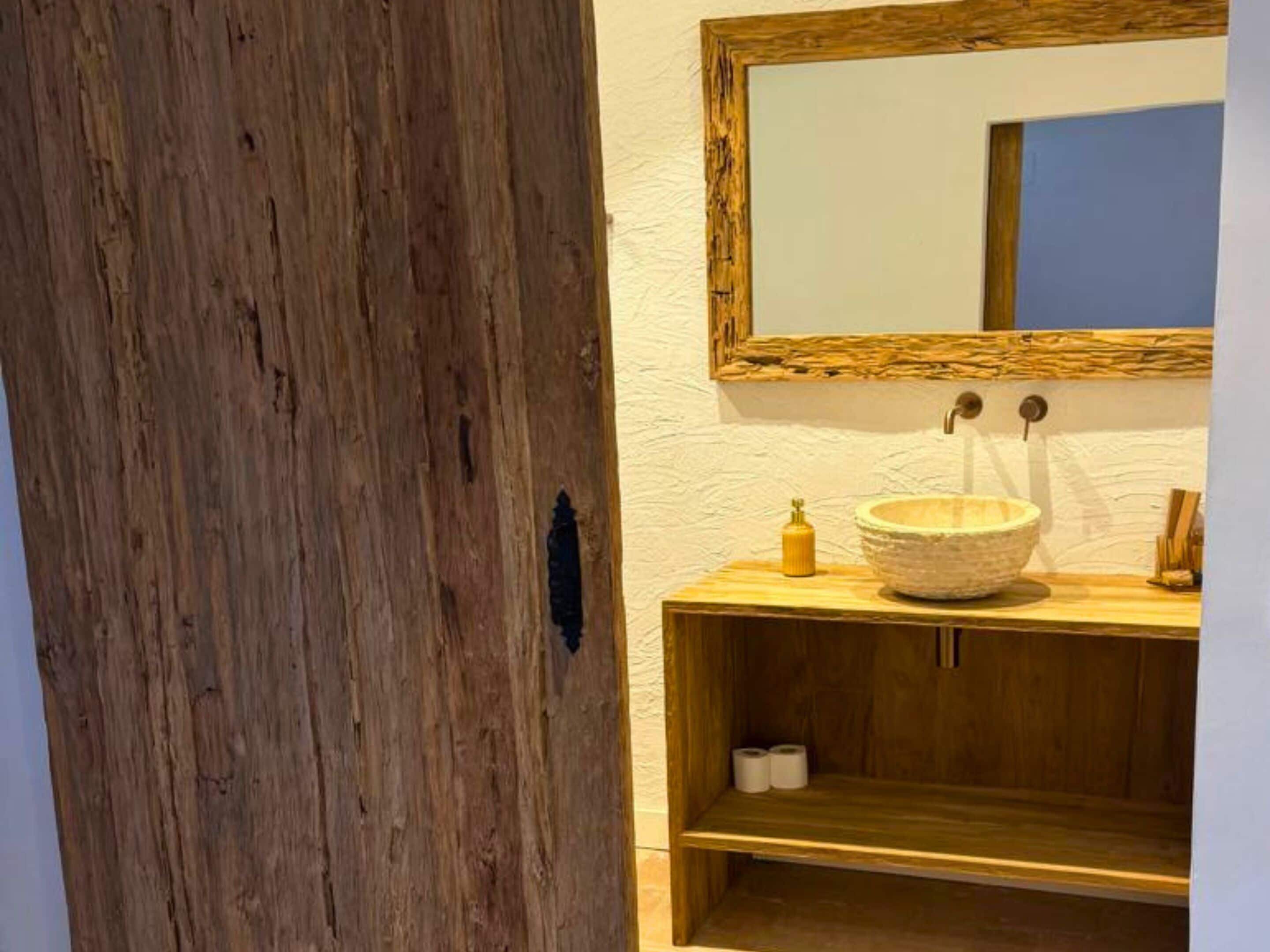 Un baño con tocador de madera, un lavabo redondo y un espejo con marco de madera.