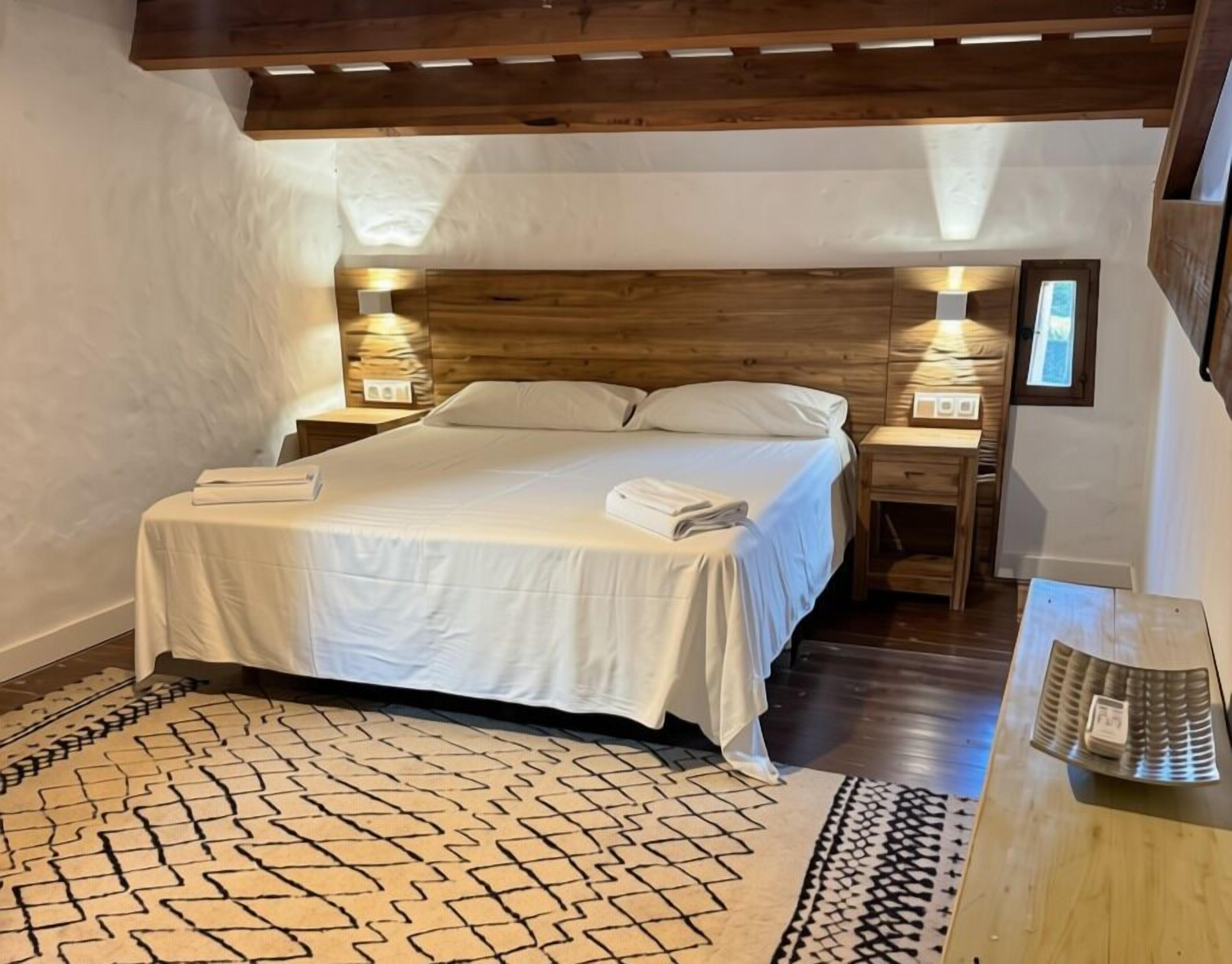 A bedroom with a bed, bedside tables, a desk, and a patterned rug.