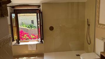 Un baño con ducha, inodoro y ventana con vistas a un jardín.